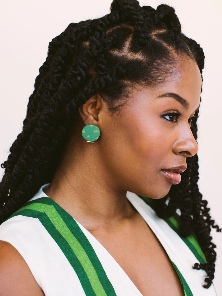 Woman wearing circular emerald green earrings with golden sundance starbursts, handmade locally in Charlotte, NC (North Carolina), at a Plaza Midwood woman owned jewelry art and home decor gift shop. A can't miss thing to do - order a housemade vegan chai at The Chai Window to sip while you shop. 