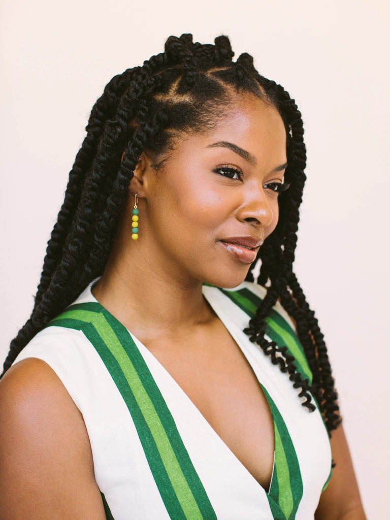 Woman wearing gold and green stacking dot earrings, handmade locally in Charlotte, NC (North Carolina), at a Plaza Midwood woman owned jewelry art and home decor gift shop. A can't miss thing to do - order a housemade vegan chai at The Chai Window to sip while you shop. 