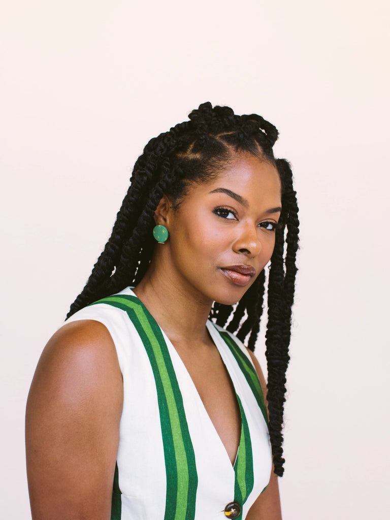 Woman wearing circular emerald green earrings with golden sundance starbursts, handmade locally in Charlotte, NC (North Carolina), at a Plaza Midwood woman owned jewelry art and home decor gift shop. A can't miss thing to do - order a housemade vegan chai at The Chai Window to sip while you shop. 