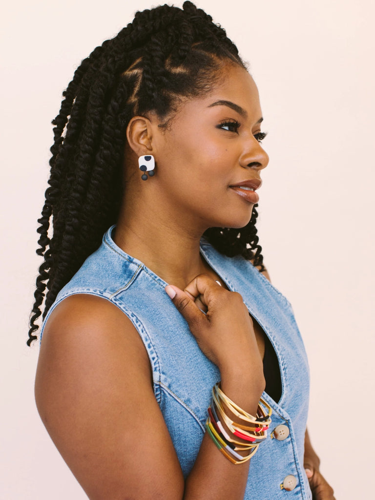 Woman wearing square earrings with black spots on a white porcelain background, handmade locally in Charlotte, NC (North Carolina), at a Plaza Midwood woman owned jewelry art and home decor gift shop. A can't miss thing to do - order a housemade vegan chai at The Chai Window to sip while you shop. 